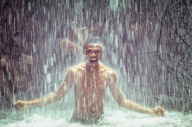Muž stojí pod vodopádom a kričí